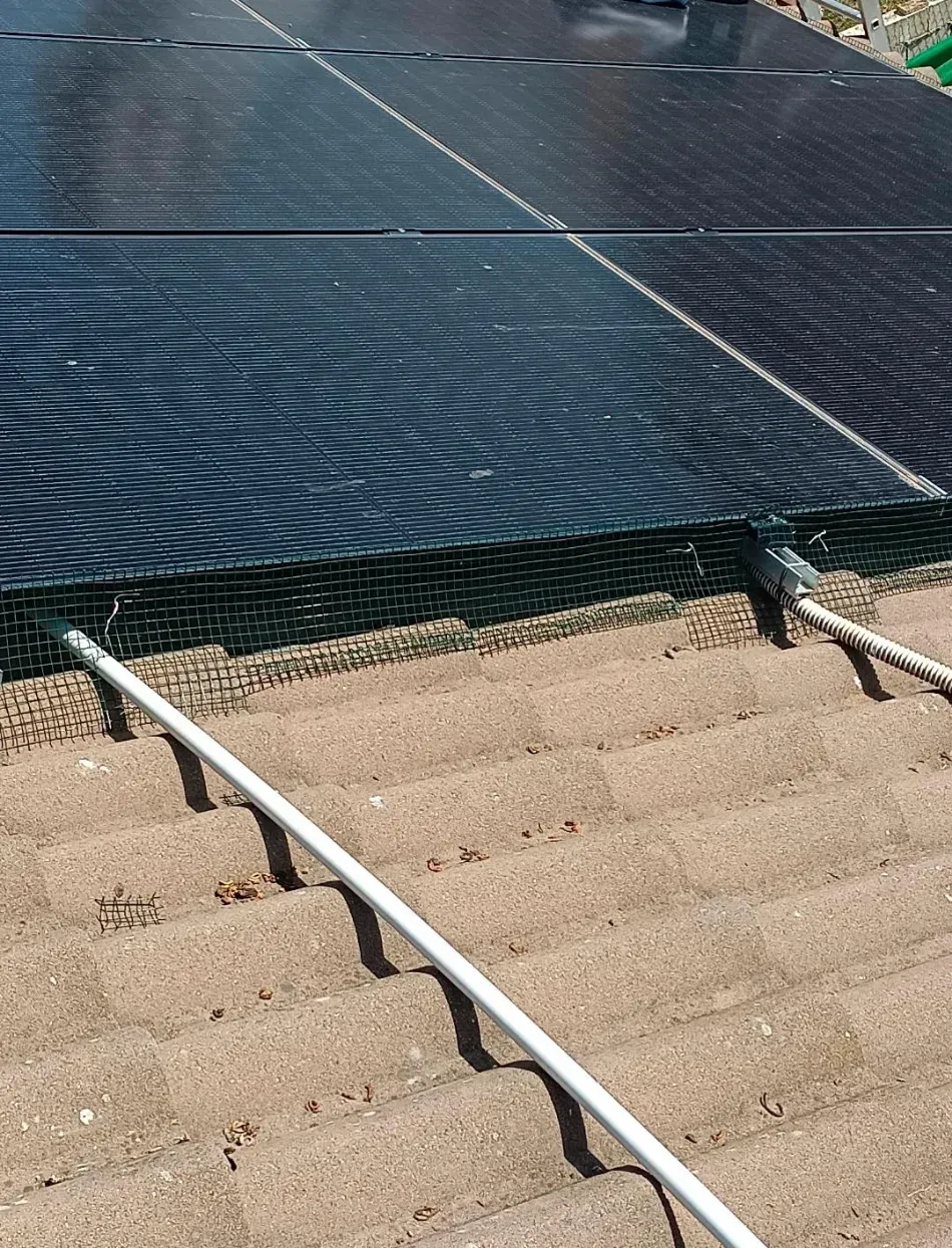 Conjunto de paneles solares sobre un tejado arenoso con dos barandillas metálicas en primer plano.