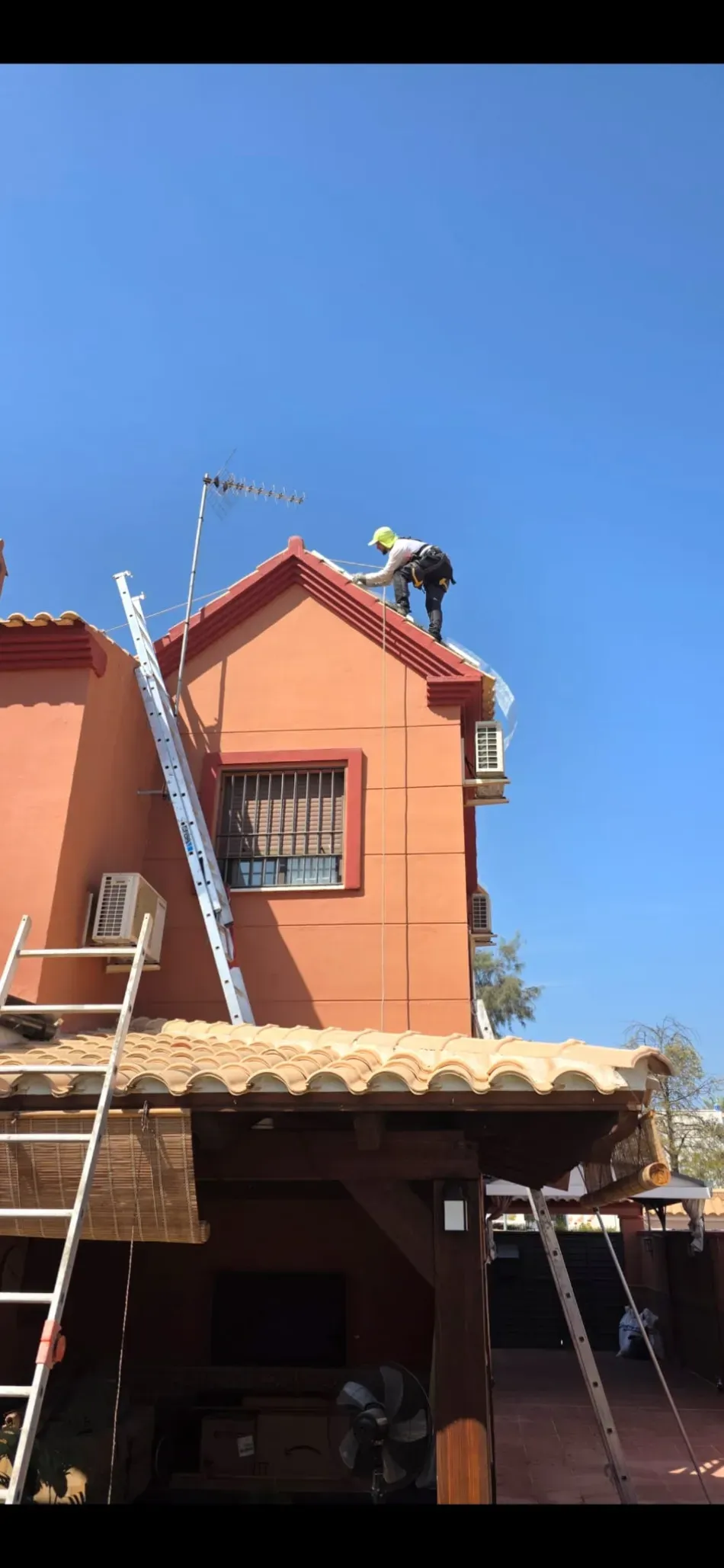 Casa naranja con escalera en el tejado y antena parabólica contra un cielo azul.