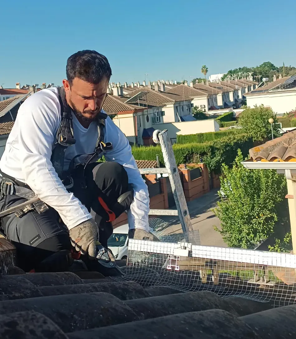 Un trabajador, agachado en un tejado, instala o repara material de cubierta negro bajo un cielo azul despejado.