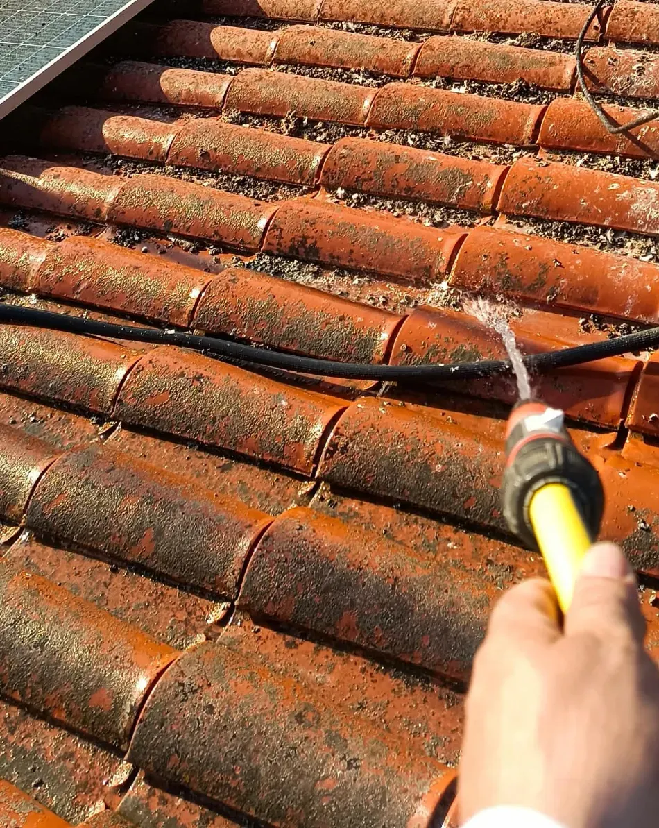 Rociar agua a mano sobre las tejas naranjas del tejado para limpiar el musgo y la suciedad.