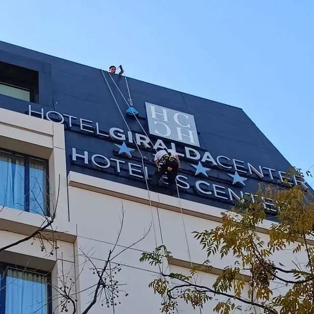 Obreros suspendidos de cuerdas reparan el letrero del 