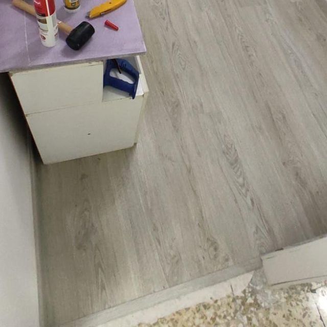 Suelo de imitación madera gris instalado en una habitación, con un armario blanco y herramientas visibles en una superficie cercana.