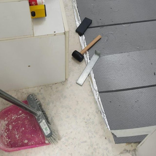 Herramientas y materiales para pisos esparcidos por el suelo, incluyendo un mazo de goma, una espátula y un nivel.