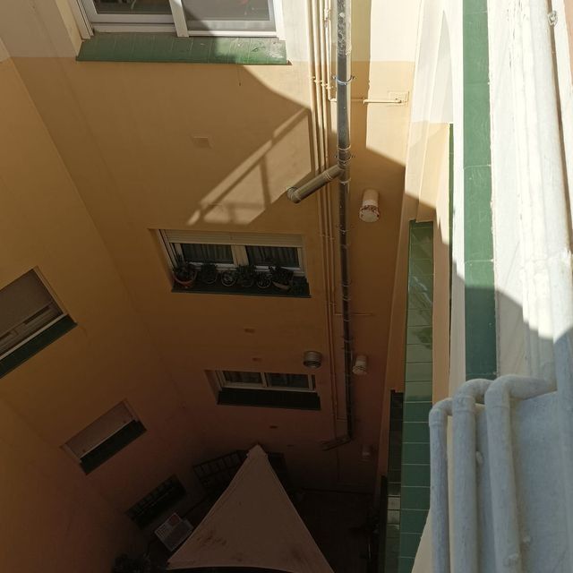 Patio estrecho del edificio con ventanas, paredes color canela y una bajante.