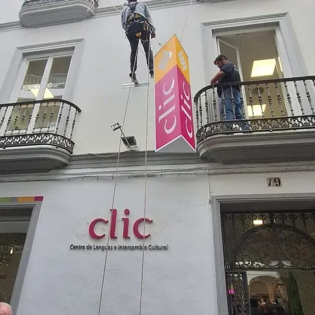 Persona suspendida de cuerdas instala un cartel para el centro de idiomas 