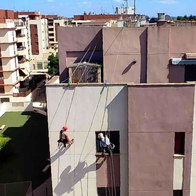 Dos personas descienden en rappel por la fachada de un edificio utilizando cuerdas. Una de ellas lleva casco.