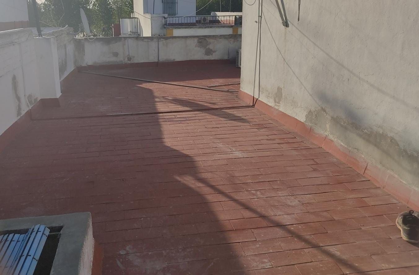 Azotea de ladrillo rojo con un muro de hormigón y un edificio al fondo.