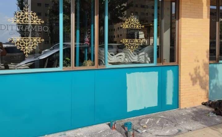 Exterior del edificio con paneles turquesa, ventanas y una mancha de pintura azul claro.