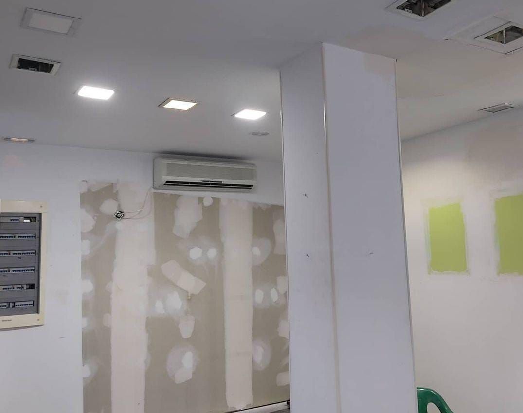 Vista interior de una habitación en construcción con paredes blancas, un pilar de soporte y luces de techo.