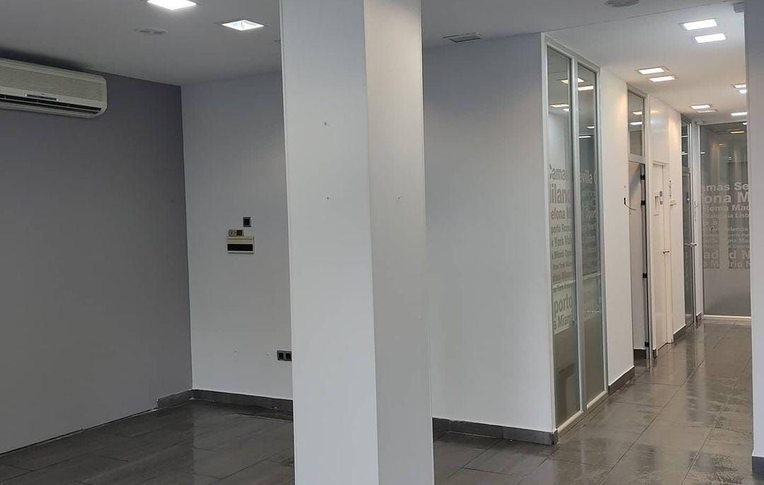 Espacio de oficina vacío con paredes grises, columnas blancas y puertas con paneles de vidrio.