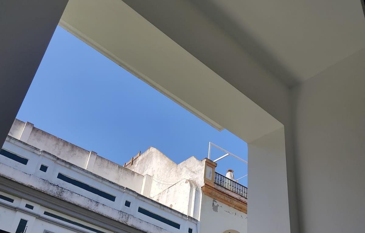 Edificio blanco enmarcado por una puerta blanca, contra un cielo azul brillante.