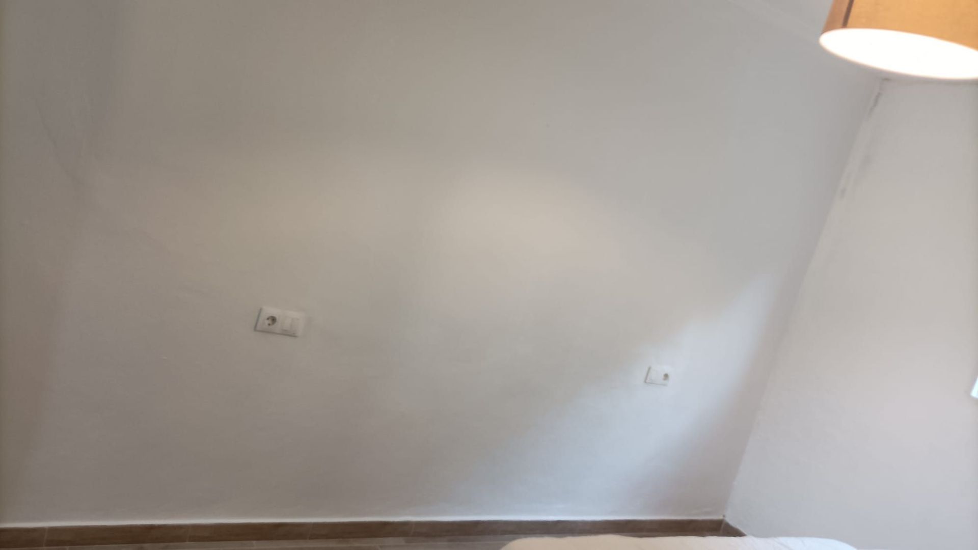 Pared blanca inclinada con enchufes eléctricos y una lámpara.
