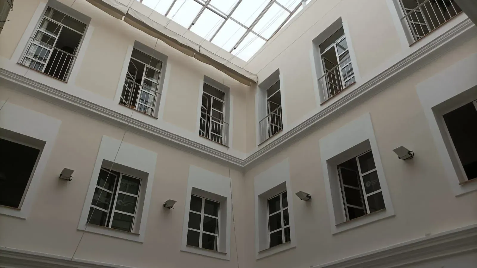 Patio interior con paredes color crema, múltiples ventanas y techo de cristal.