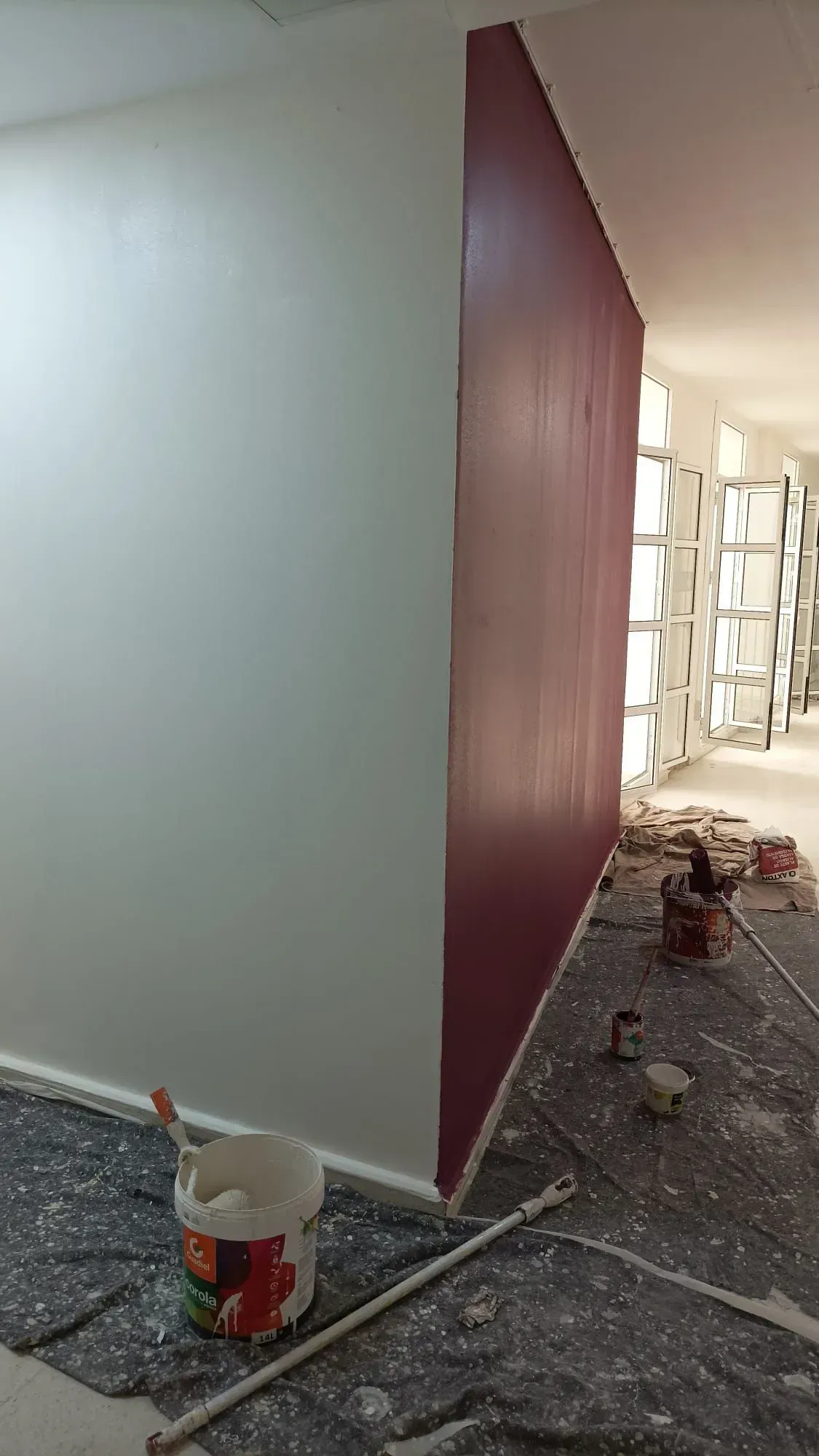 Pared interior pintada de blanco, pared contigua de rojo intenso. Materiales de pintura en el suelo.