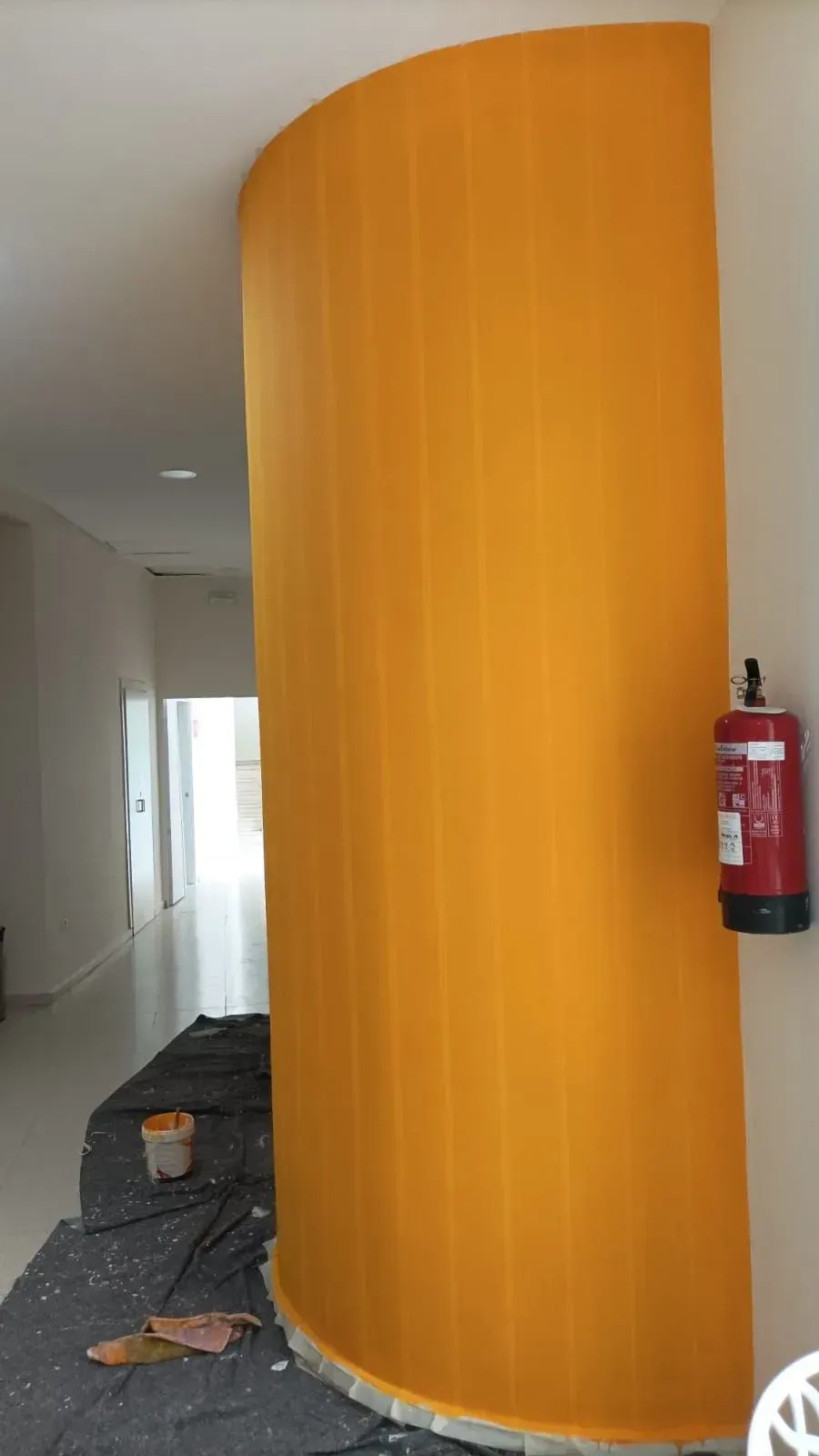 Pared curva pintada de naranja en un pasillo interior; un extintor está montado en la pared adyacente.