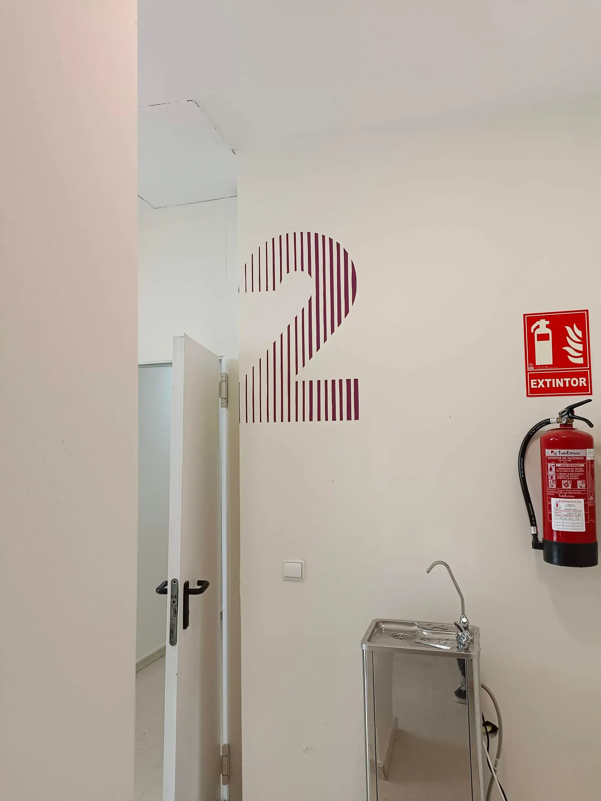 Habitación con puerta, calcomanía con el número 2, extintor y fuente de agua.