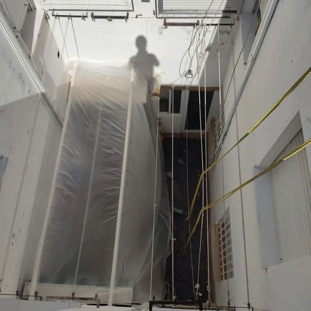 La sombra de una persona sobre una estructura con láminas de plástico transparente, cuerdas y ventanas.