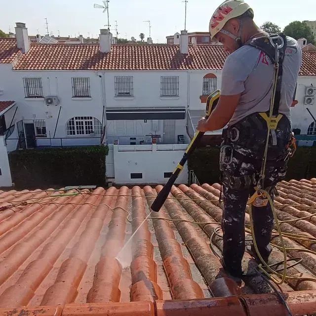 Hombre con equipo de seguridad lavando a presión un tejado de tejas rojas.