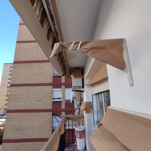 Un papel marrón cubre el toldo de un balcón. Al fondo se ven un edificio y el cielo azul.