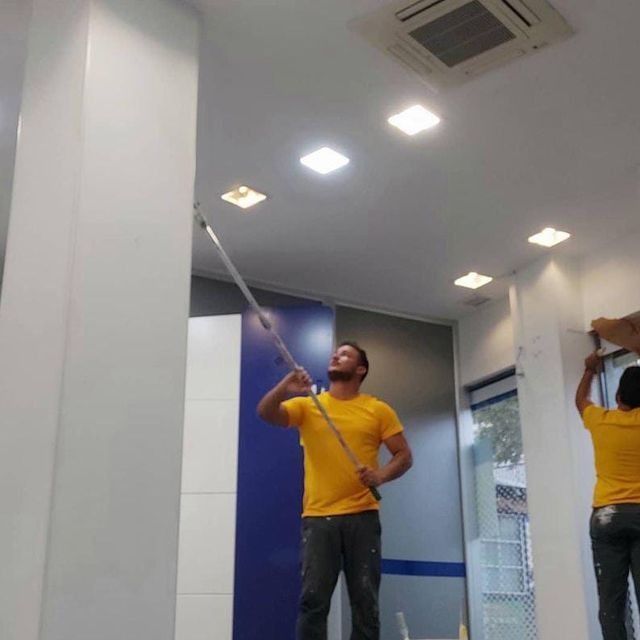 Dos personas pintando el techo de una habitación. Una usa un rodillo, la otra una brocha.