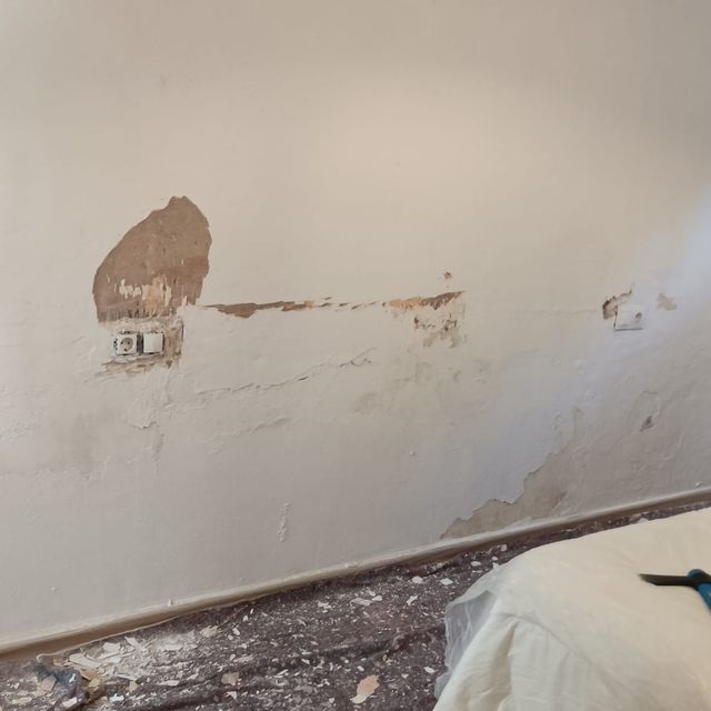 Pared interior dañada con pintura desconchada, dejando al descubierto el yeso y la toma de corriente.