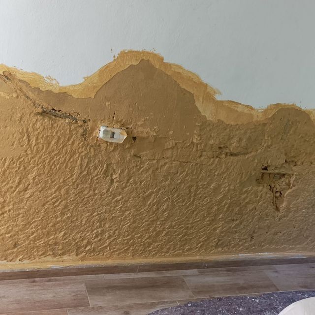 Daños en la pared con capas expuestas de yeso marrón texturizado y una toma de corriente.