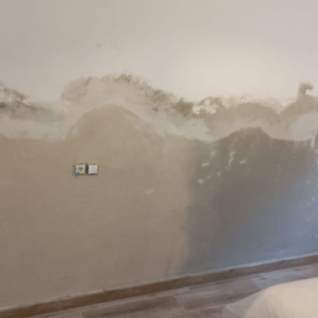 Pared con daños visibles por agua, decoloración y posible crecimiento de moho. Toma de corriente presente.