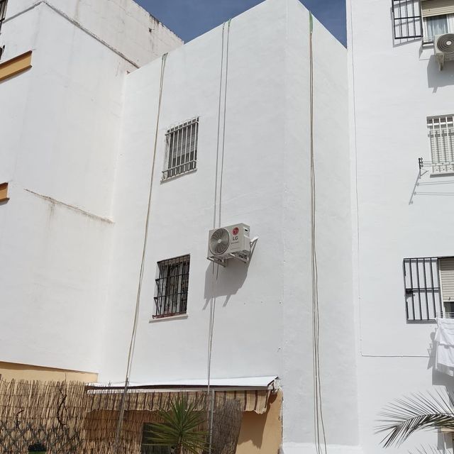 Exterior de edificio de apartamentos blanco con unidad de aire acondicionado y ventanas enrejadas.