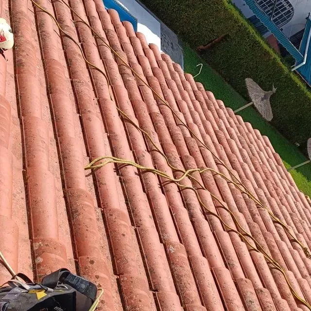 Tejado de tejas de arcilla roja con cordón amarillo que lo atraviesa; edificio azul y blanco al fondo.