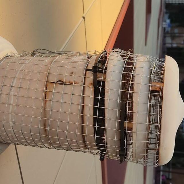 Estructura cilíndrica envuelta en malla metálica y aislamiento, montada en un edificio. Algunas secciones muestran oscurecimiento y desgaste.