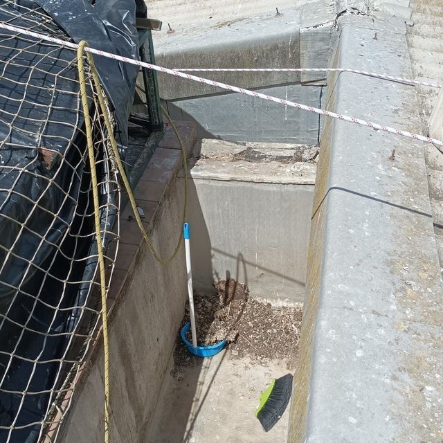 Canaleta de hormigón con escombros y productos de limpieza. Malla negra y cinta de advertencia.