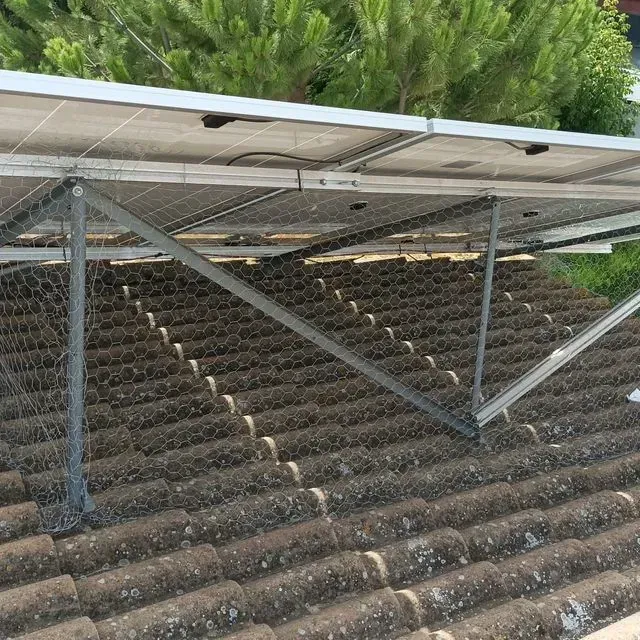 Paneles solares montados sobre un tejado de tejas con malla metálica, sostenidos por una estructura metálica.