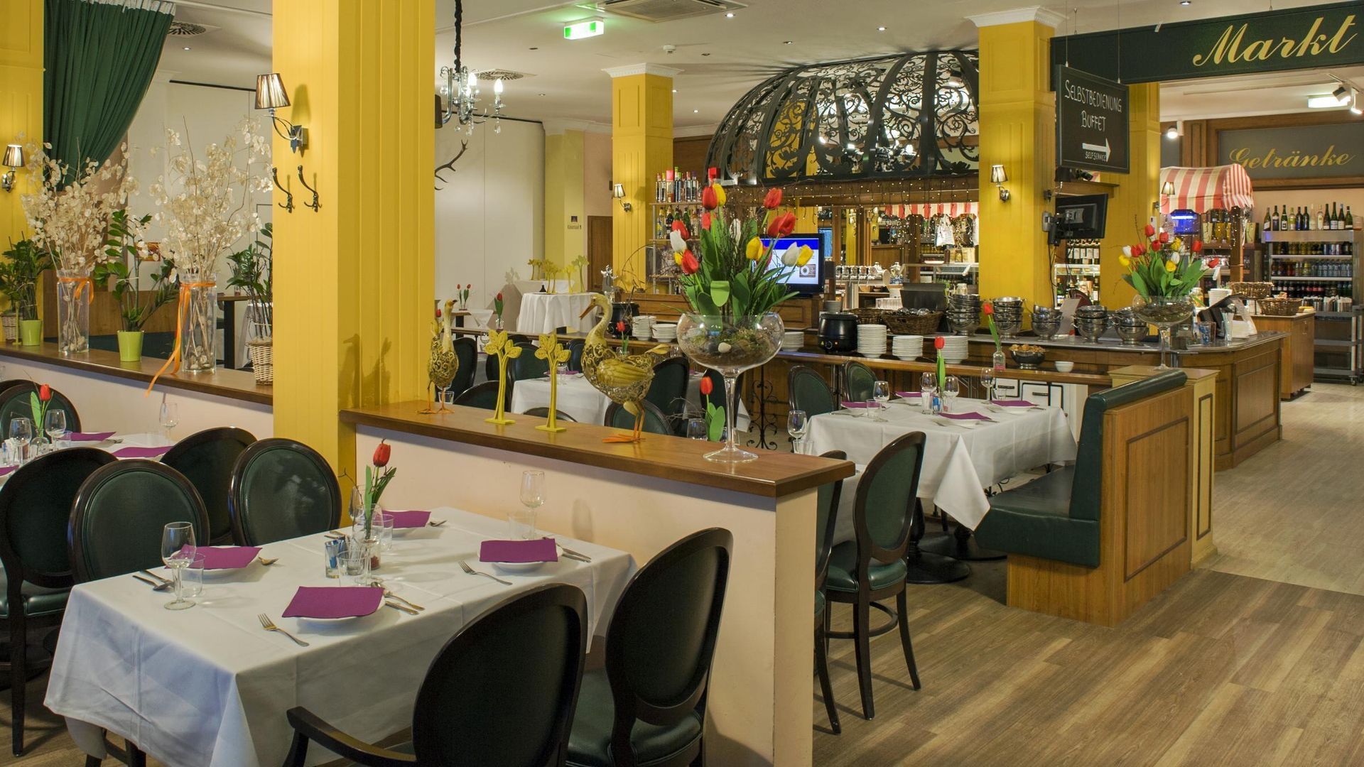 Bright restaurant interior with yellow columns, set dining tables, and a bar stocked with bottles