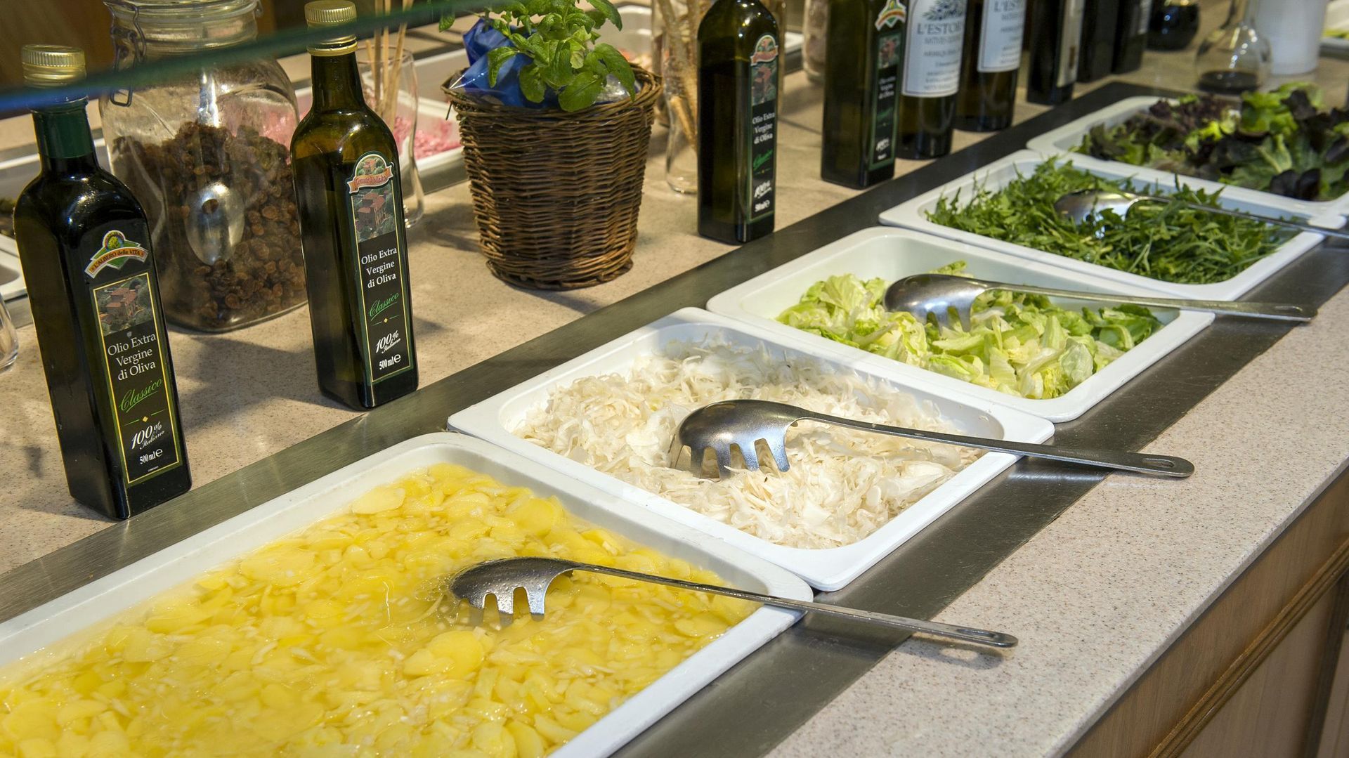 Buffet salad bar with trays of pasta, greens, and toppings on a countertop