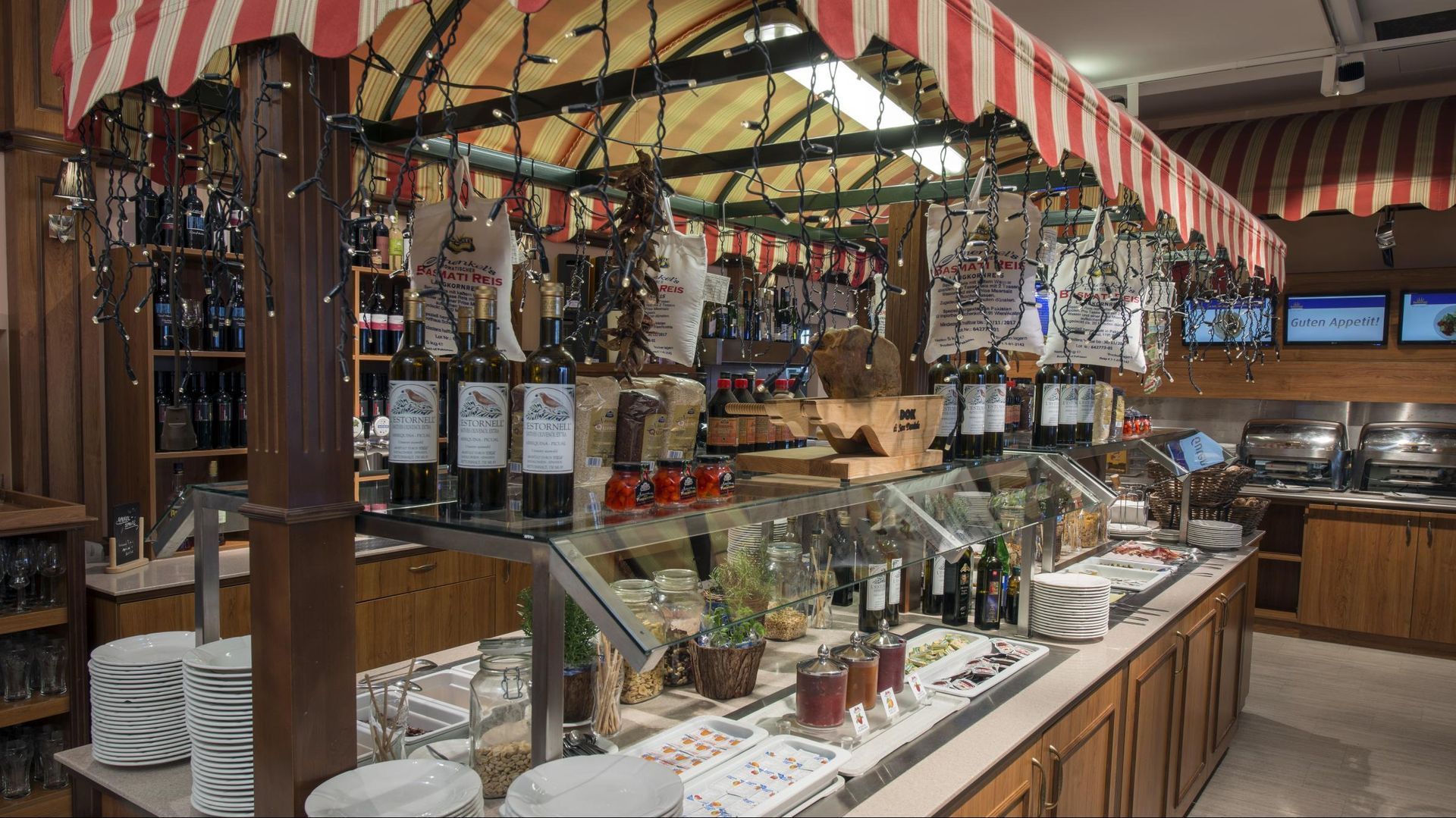 Market stall with wine bottles, hanging decorations, and a striped awning over a deli counter