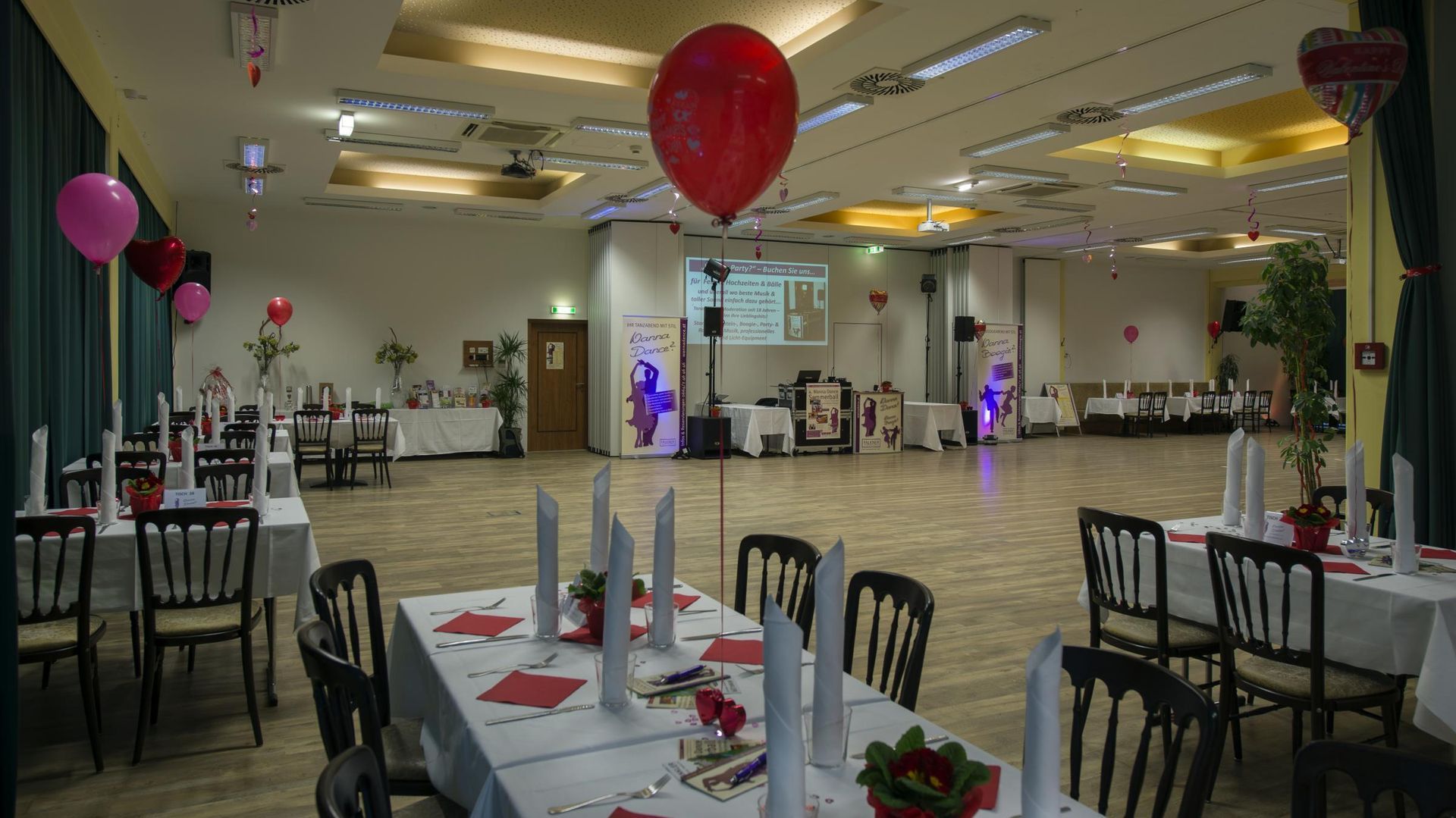Decorated banquet hall with set tables, black chairs, and red balloons