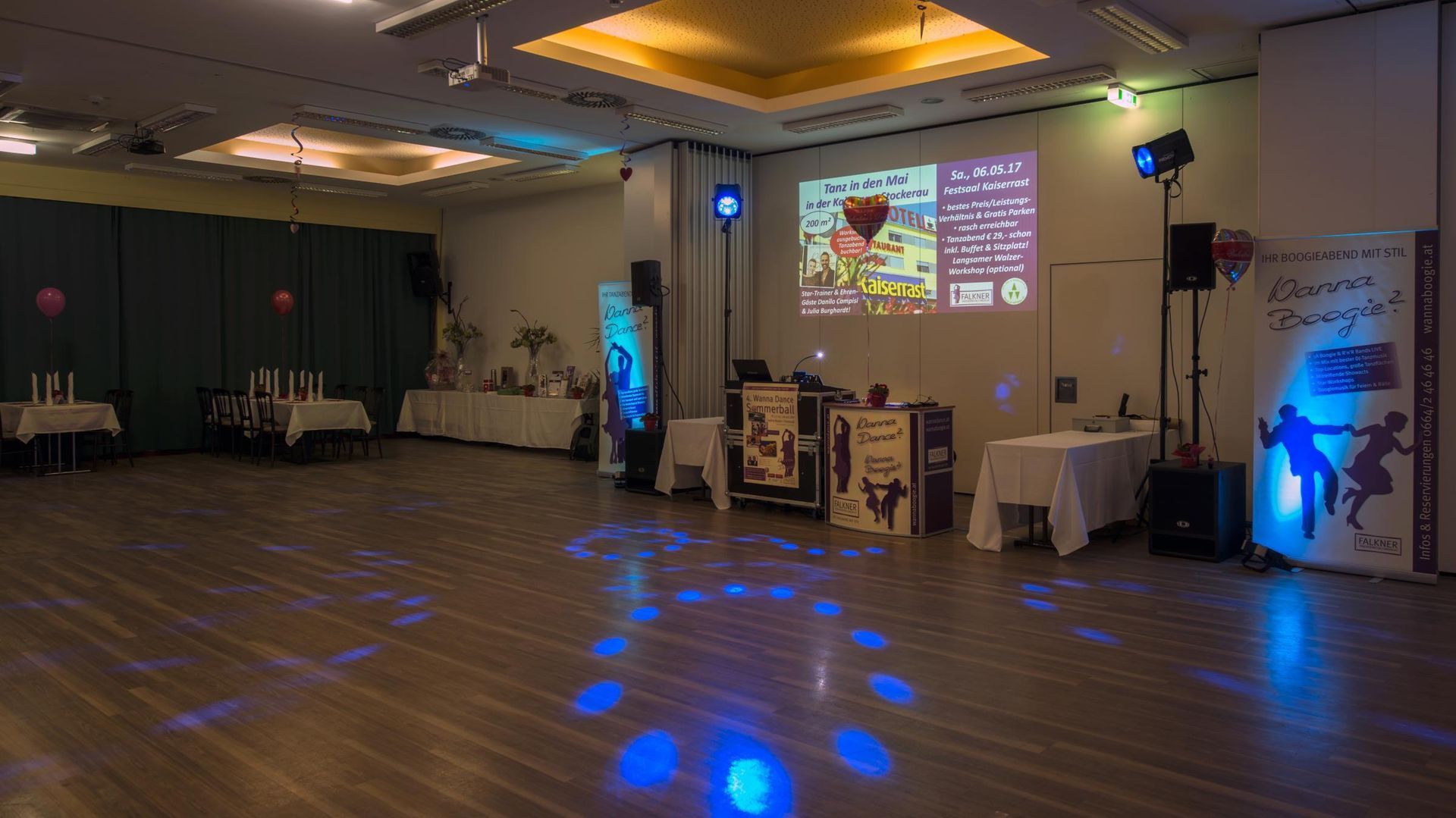 Dim event hall with blue uplights, a projected screen, and audio equipment set up near the wall.