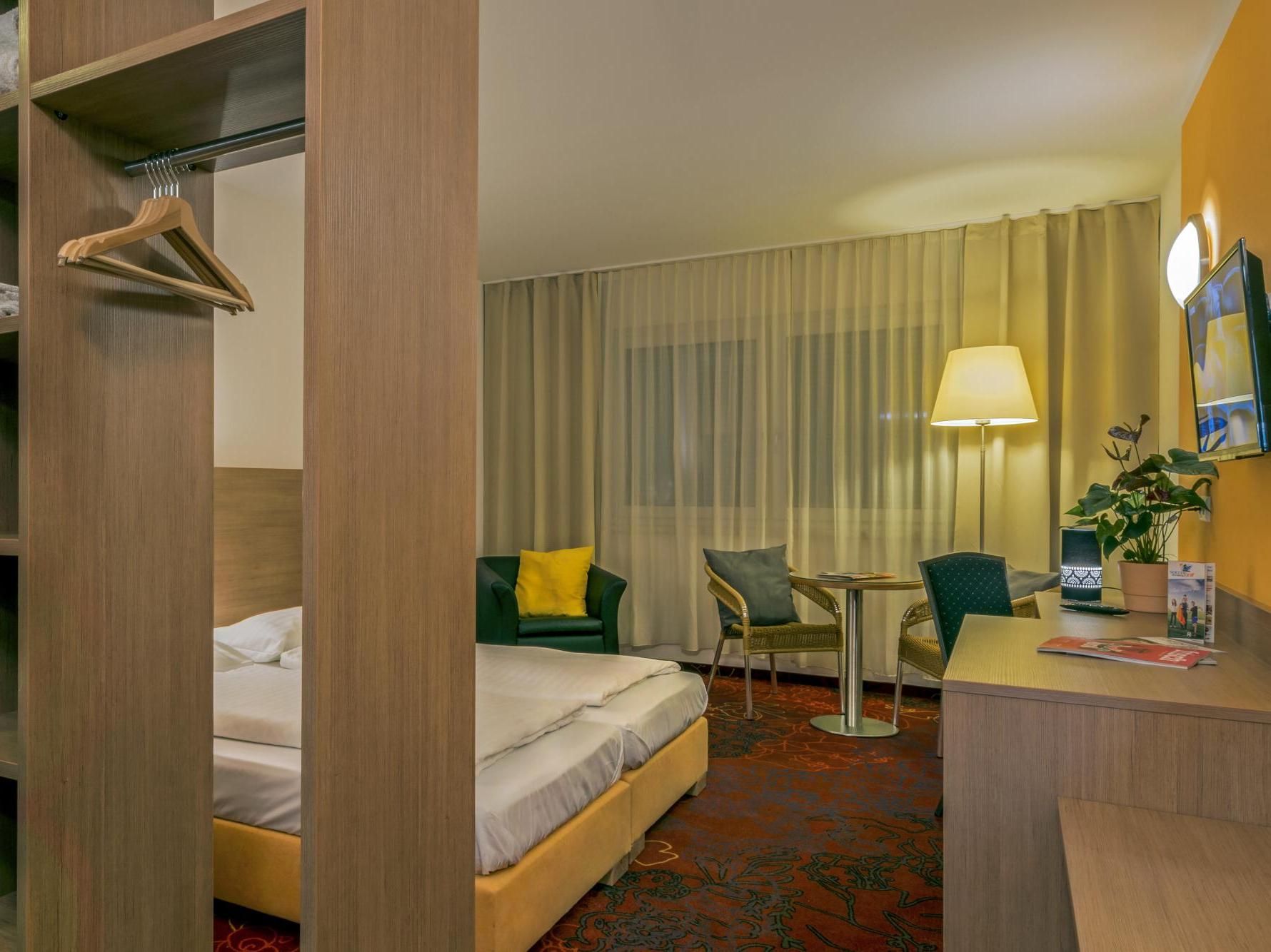 Hotel room with bed, sofa, desk, lamp, and TV in a modern beige interior
