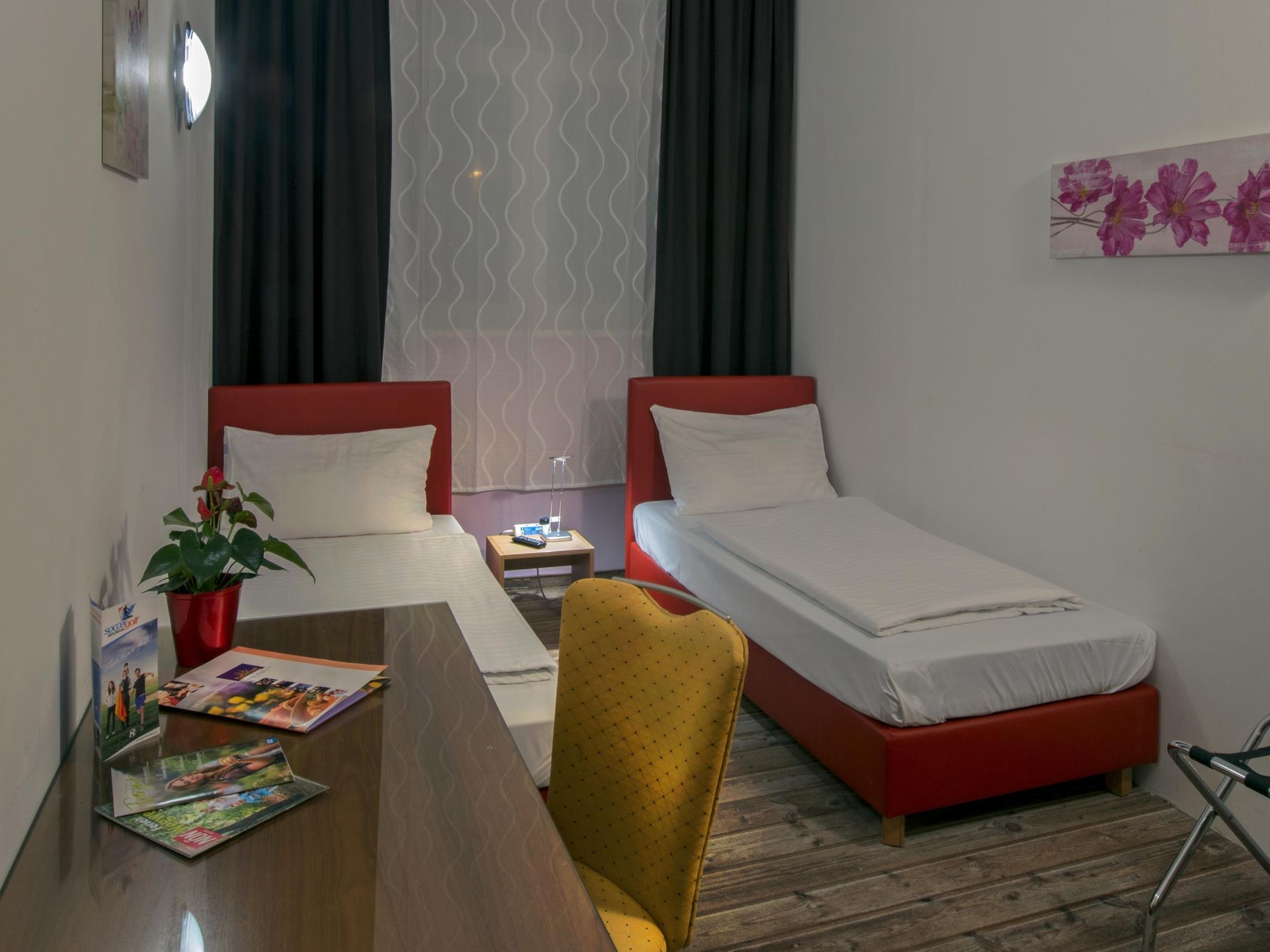 Small bedroom with two single beds, a desk, a chair, and a flower painting on the wall.