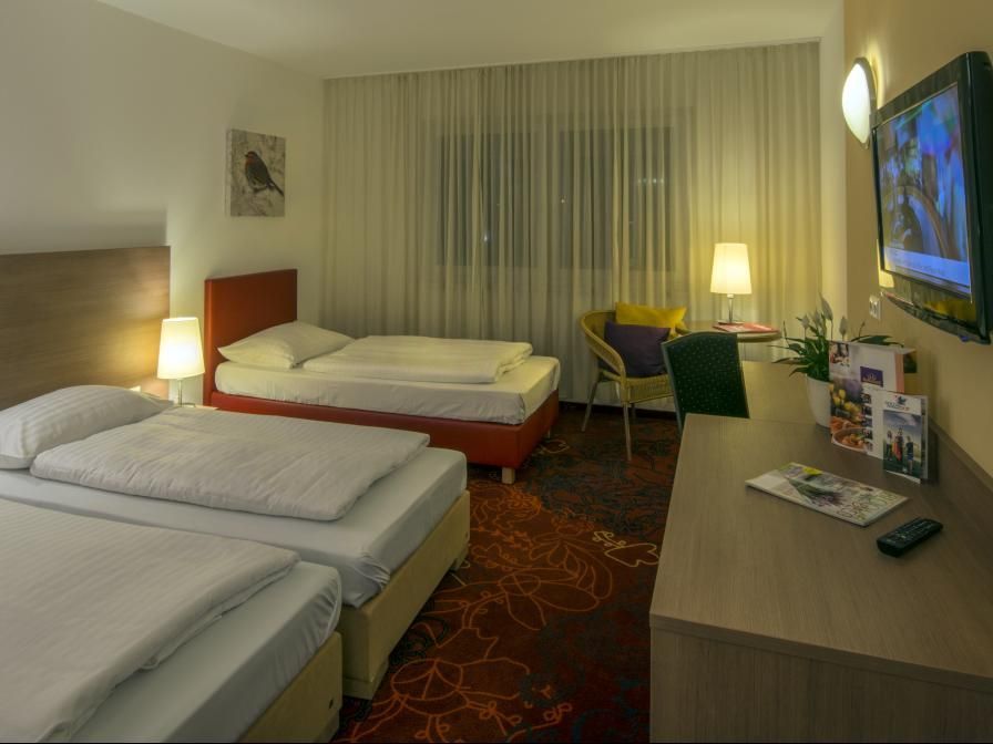 Hotel room with two beds, desk, lamp, and wall-mounted TV in warm lighting