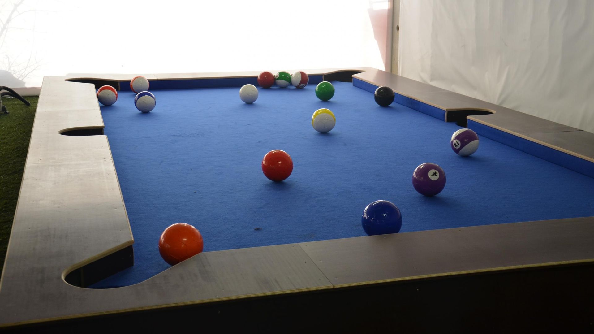 Billiards table with scattered colored pool balls on blue felt in a dimly lit room
