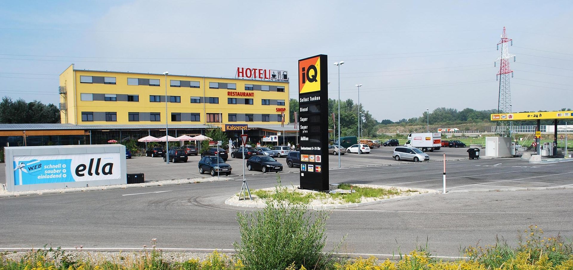 Wide view of a gas station and parking lot beside a yellow commercial building under a clear sky