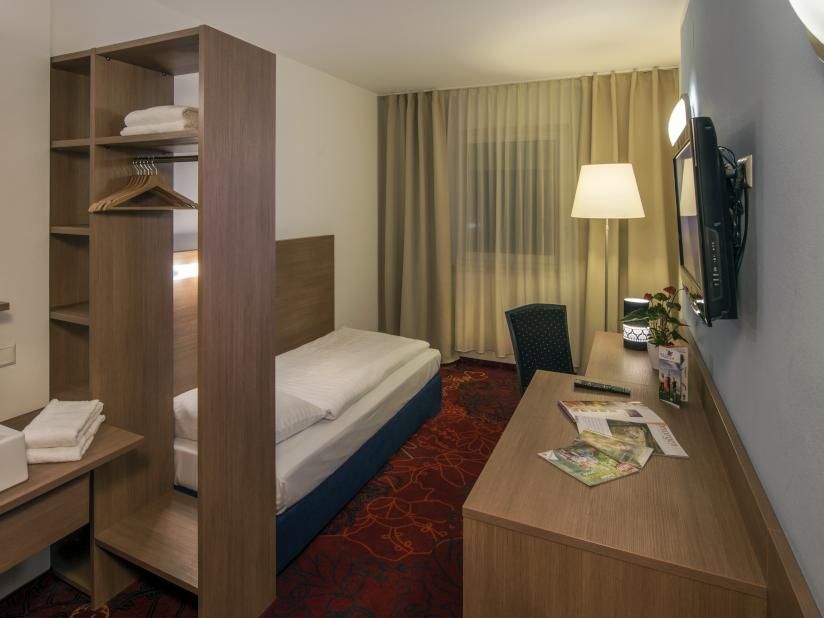 Small hotel room with single bed, desk, lamp, and red patterned rug