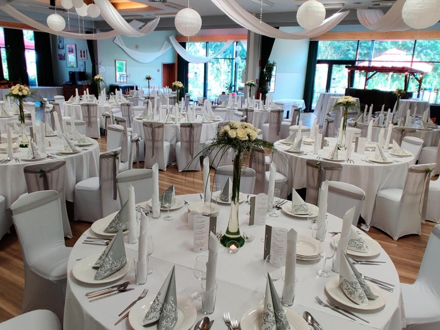 Elegant banquet hall with round white-clothed tables, tall centerpieces, and hanging white lanterns