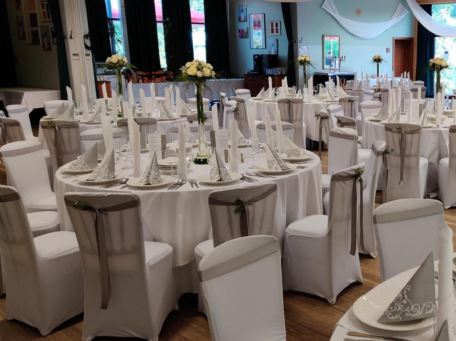 Banquet hall with round white-clothed tables, white chairs, and floral centerpieces set for an event