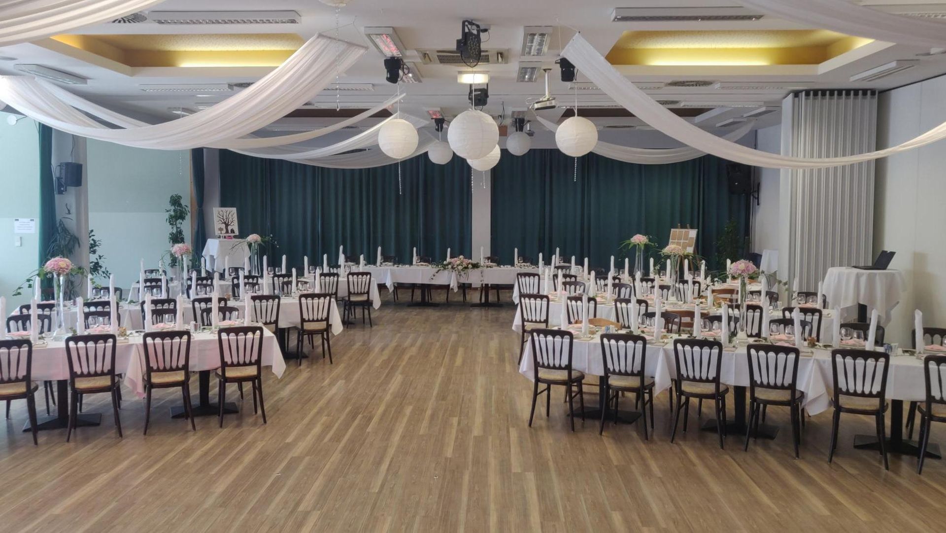 Decorated banquet hall with round tables, white chairs, and draped ceiling fabric