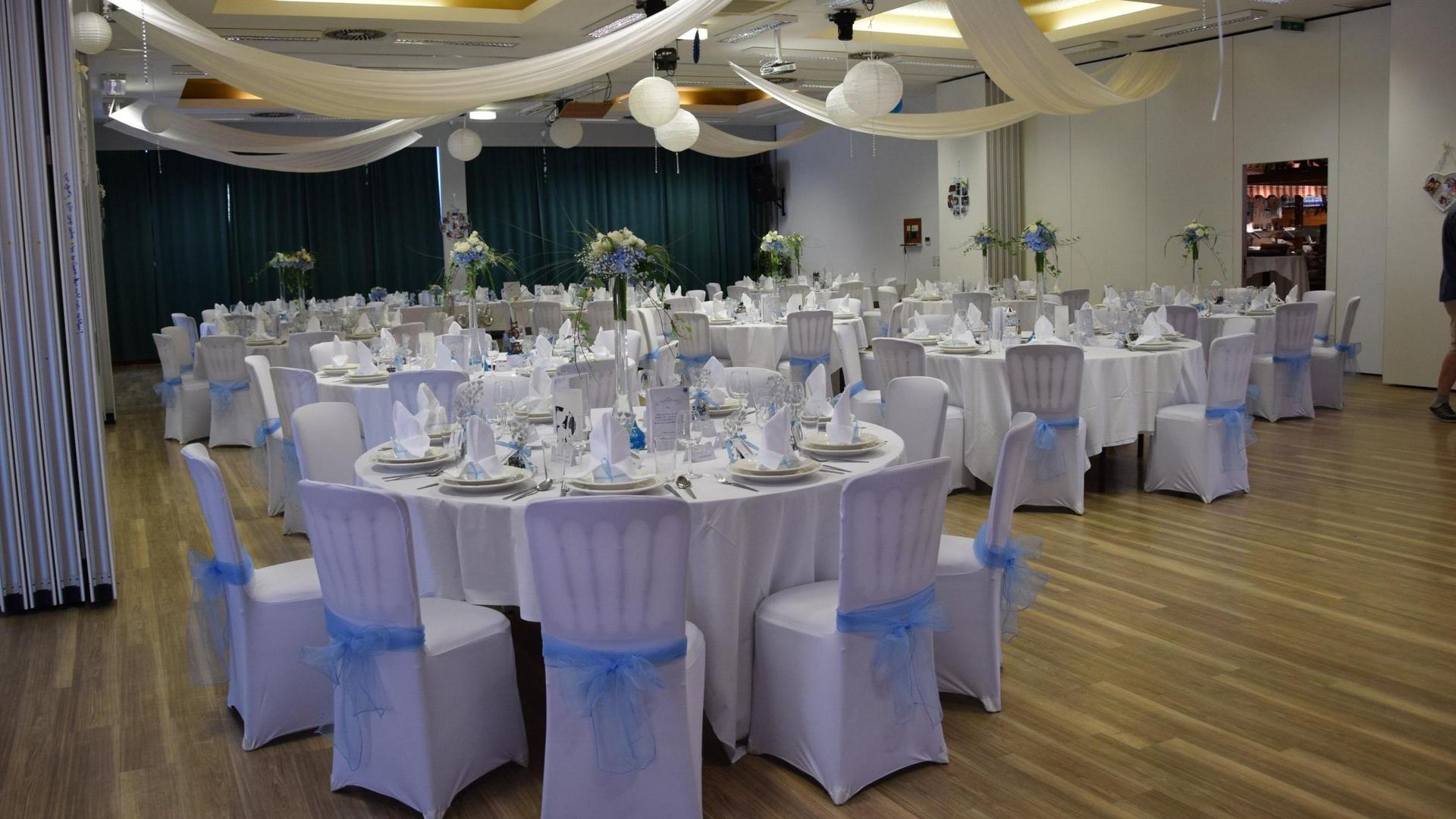 Decorated banquet hall with round, white-clothed tables set for an event