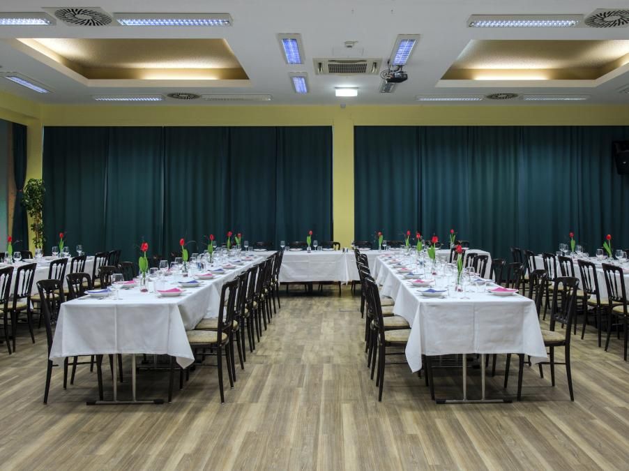 Empty banquet hall with long white-clothed tables and black chairs under ceiling lights