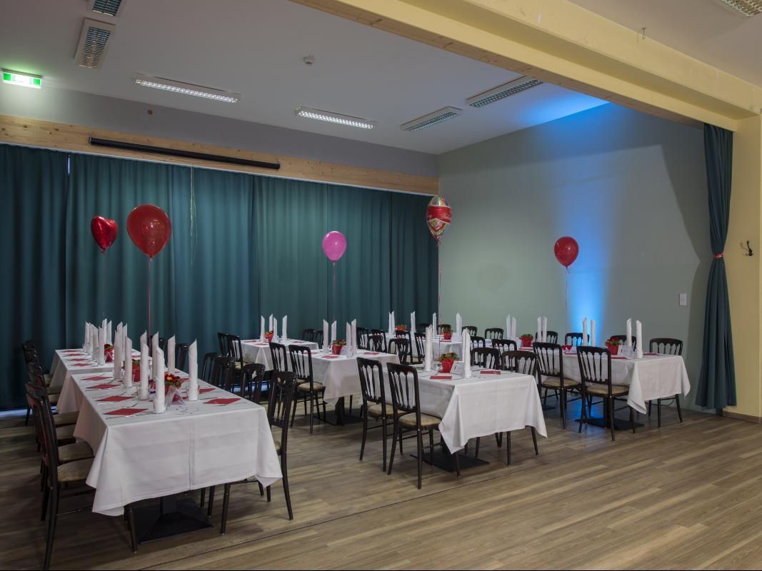 Decorated event hall with tables, chairs, blue curtains, and red and pink balloons