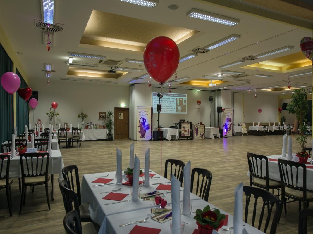 Decorated banquet hall with tables, chairs, red balloons, and a projector screen at the front
